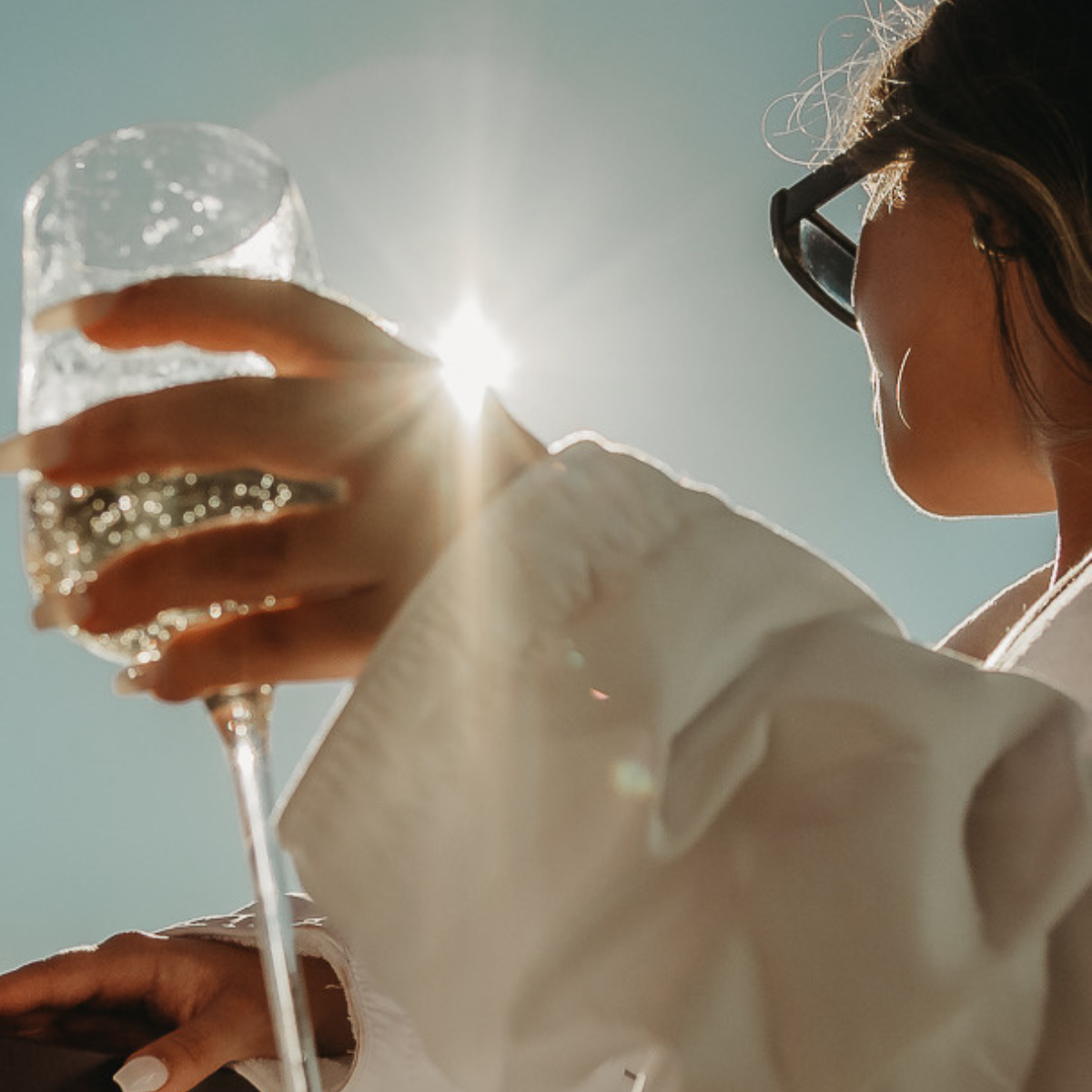 Person holding a sparkling wine glass with sunlight in the background