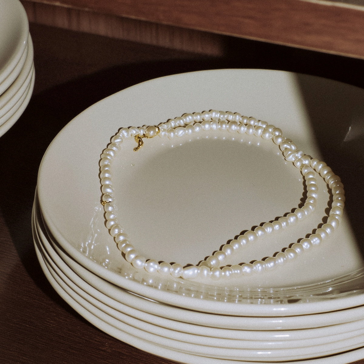 Stack of white plates with a pearl necklace on top
