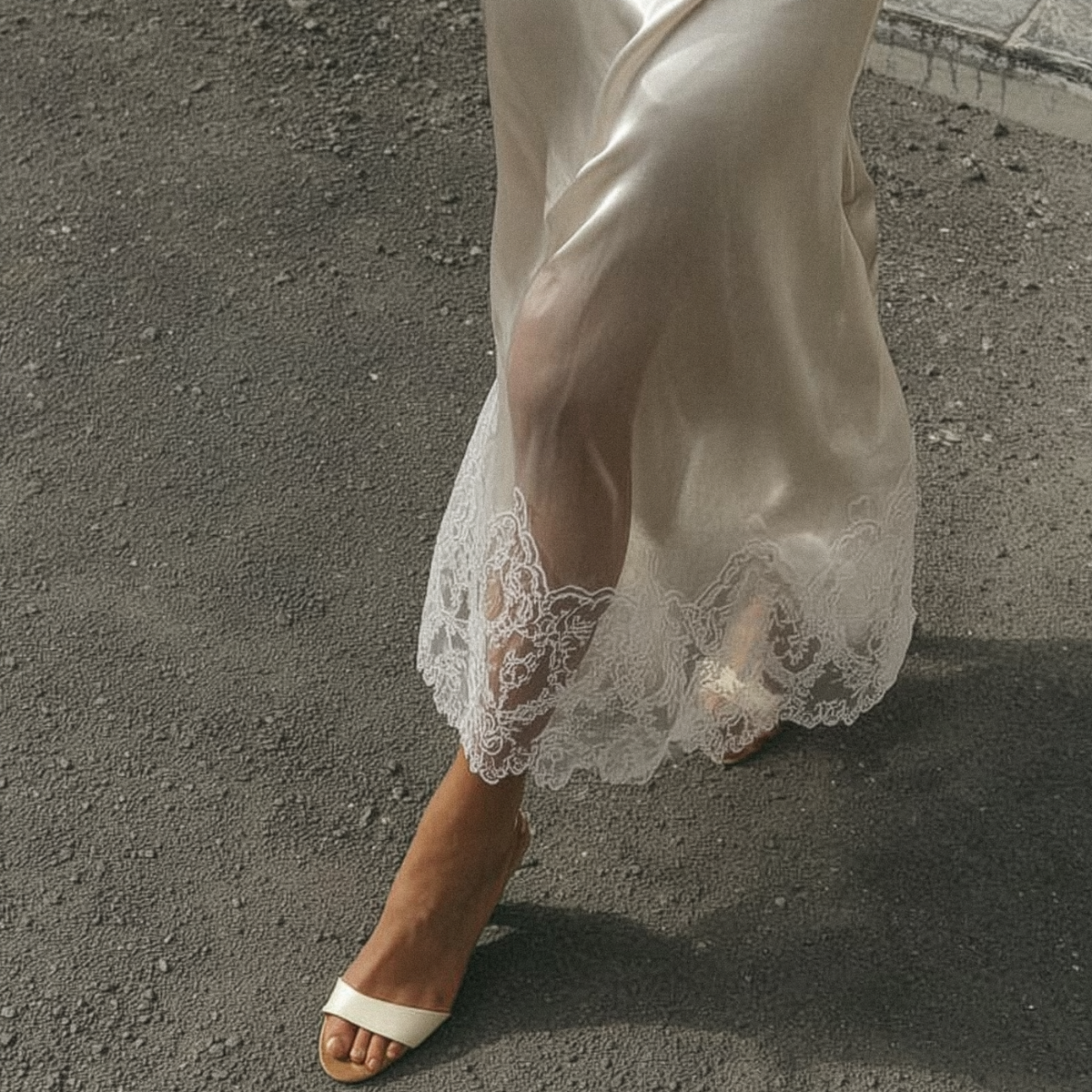 Person wearing a sheer white lace dress with sandals on a textured surface