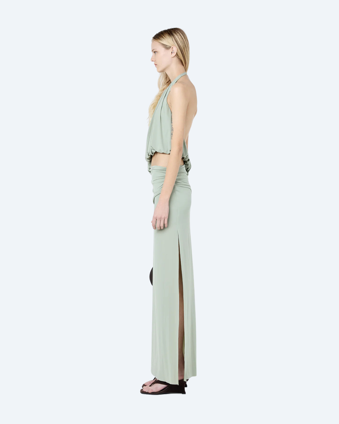 Woman wearing a pistachio Bec & Bridge Cadence Racer, backless, maxi dress, side view, on a white background